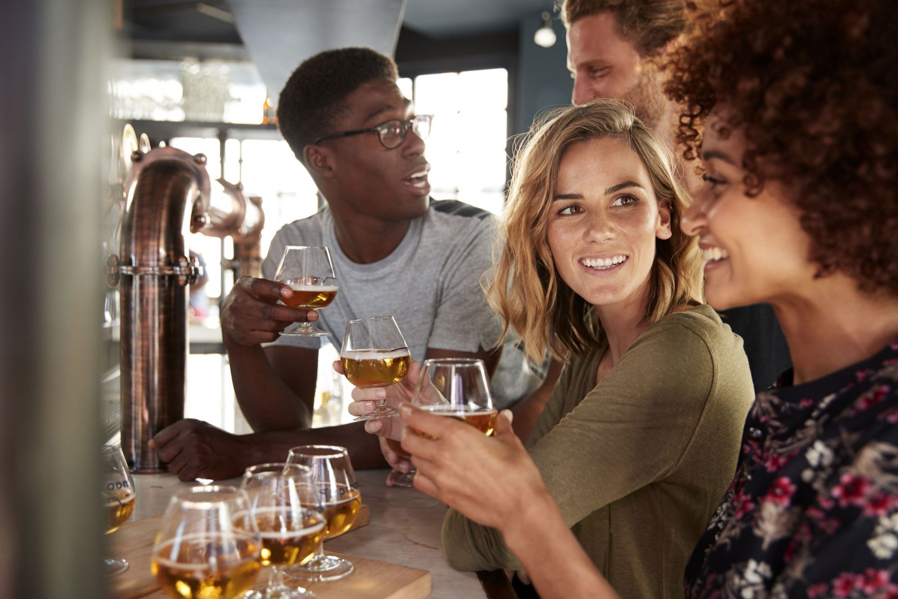 Four friends enjoying drinks and conversation at a bar in Asheville, North Carolina, holding glasses of beer and smiling at each other.