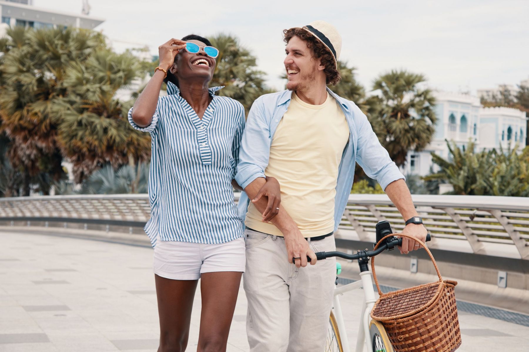 Two men walking a bicycle while arm in arm on a beachside walkway