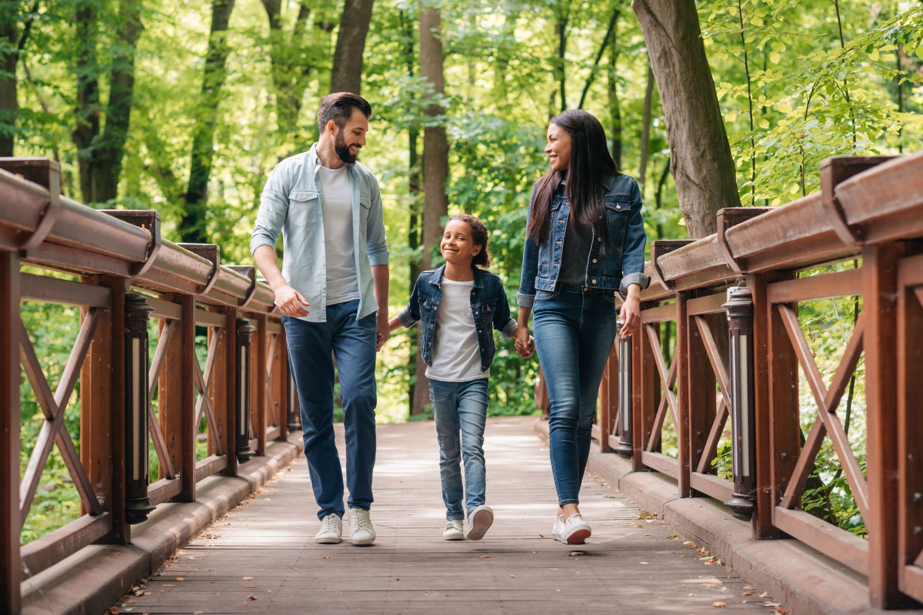 A family of three, walking and smiling on a wooden bridge in a lush, green forest in Asheville, North Carolina.