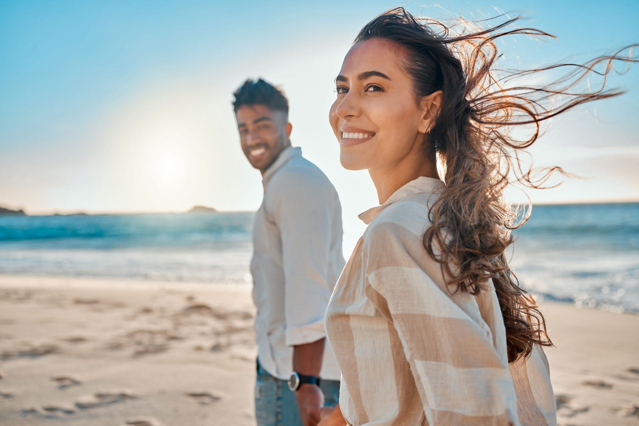 A happy couple holding hands while walking along the beach on a sunny day